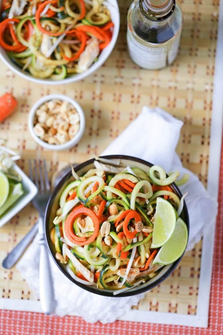 An overhead photo of a bowl of pad thai made with zucchini noodles with two lime wedges. 