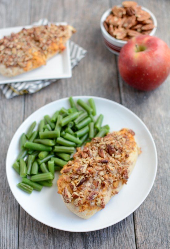 A white plate with apple pecan chicken breast with green beans.