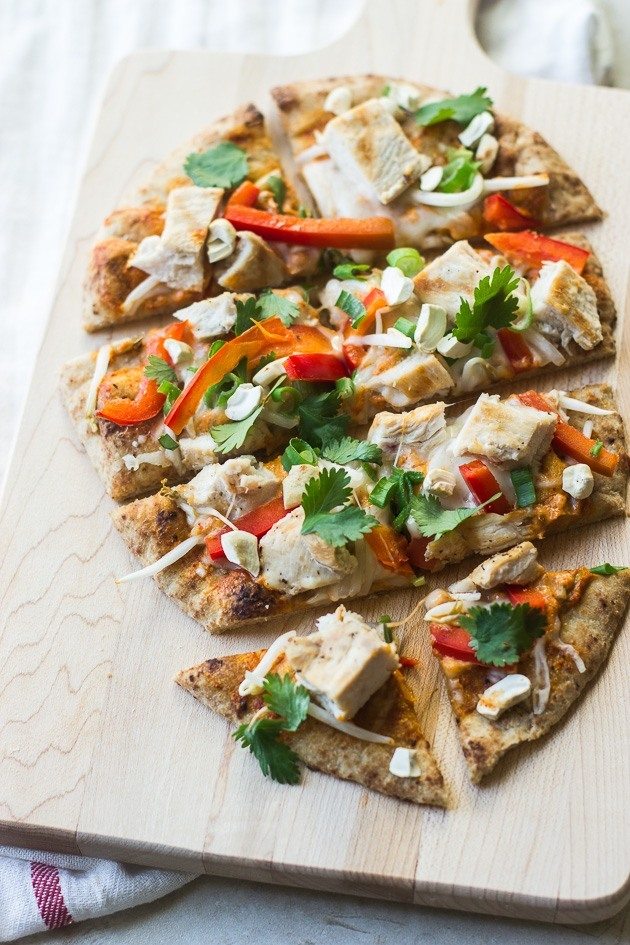 A naan pizza with chicken, bell pepper, and herbs, sliced.