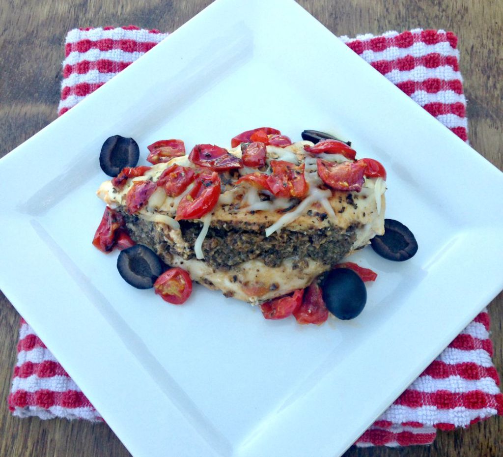 A white plate with a tapenade stuffed chicken.