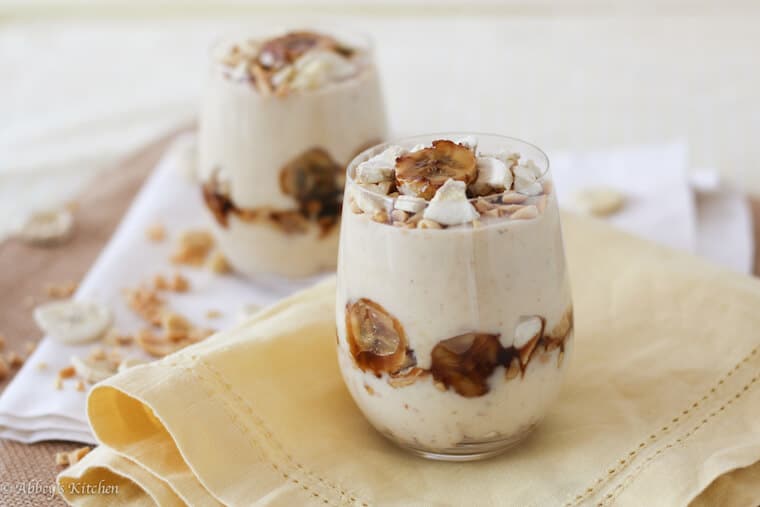 A photo of a glass of banana protein pudding with banana garnished on top in focus with a second one in the background.