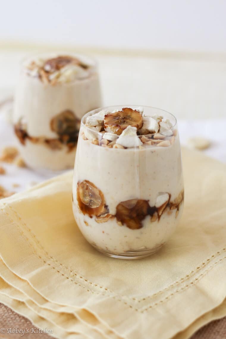 A photo of a glass of banana protein pudding with banana garnished on top in focus with a second one in the back.