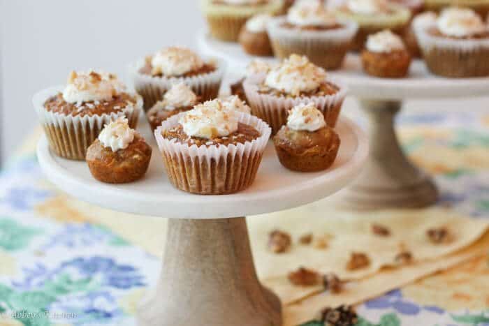 A cake stand with multiple regular sized carrot cake cupcakes with a few mini ones.