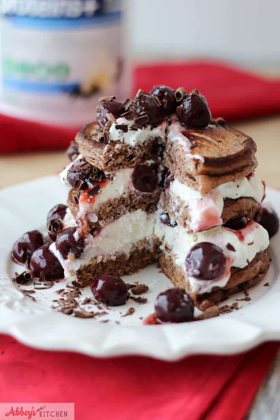 stack of chocolate and cherry protein pancakes with whipped cream and chocolate shavings on a white plate