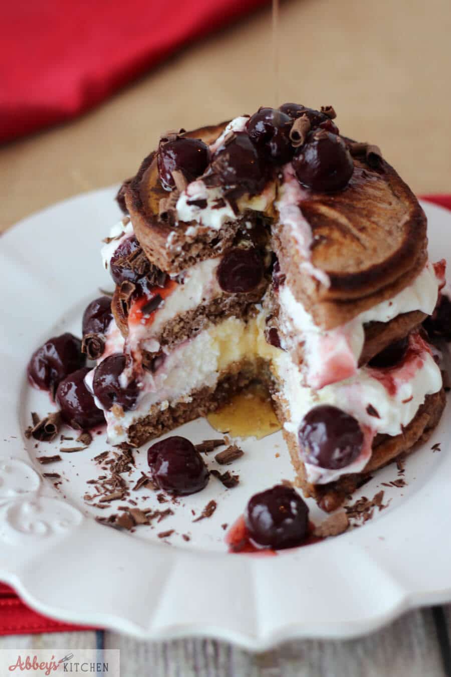 stack of chocolate protein pancakes with whipped cream, cherries, and shaved chocolate on a white plate