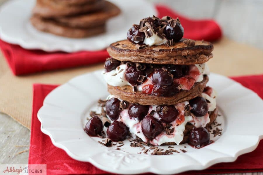 stack of black forest protein pancakes with whipped cream and cherries on a white plate