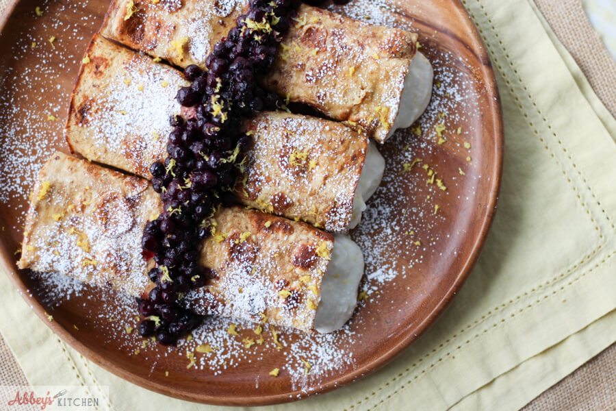 An overhead photo of a plate of three cheesecake stuffed french toast crepes.