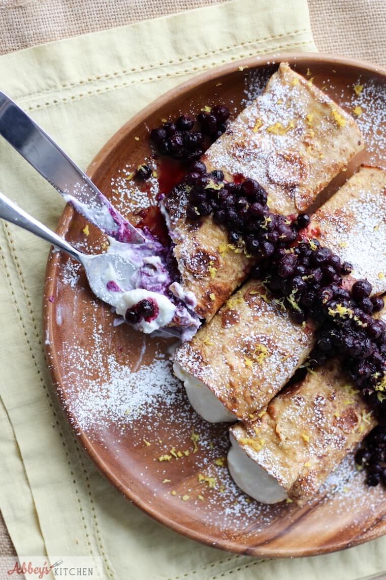 An overhead photo of plate of cheesecake stuffed french toast crepes with a knife and fork cutting into it.