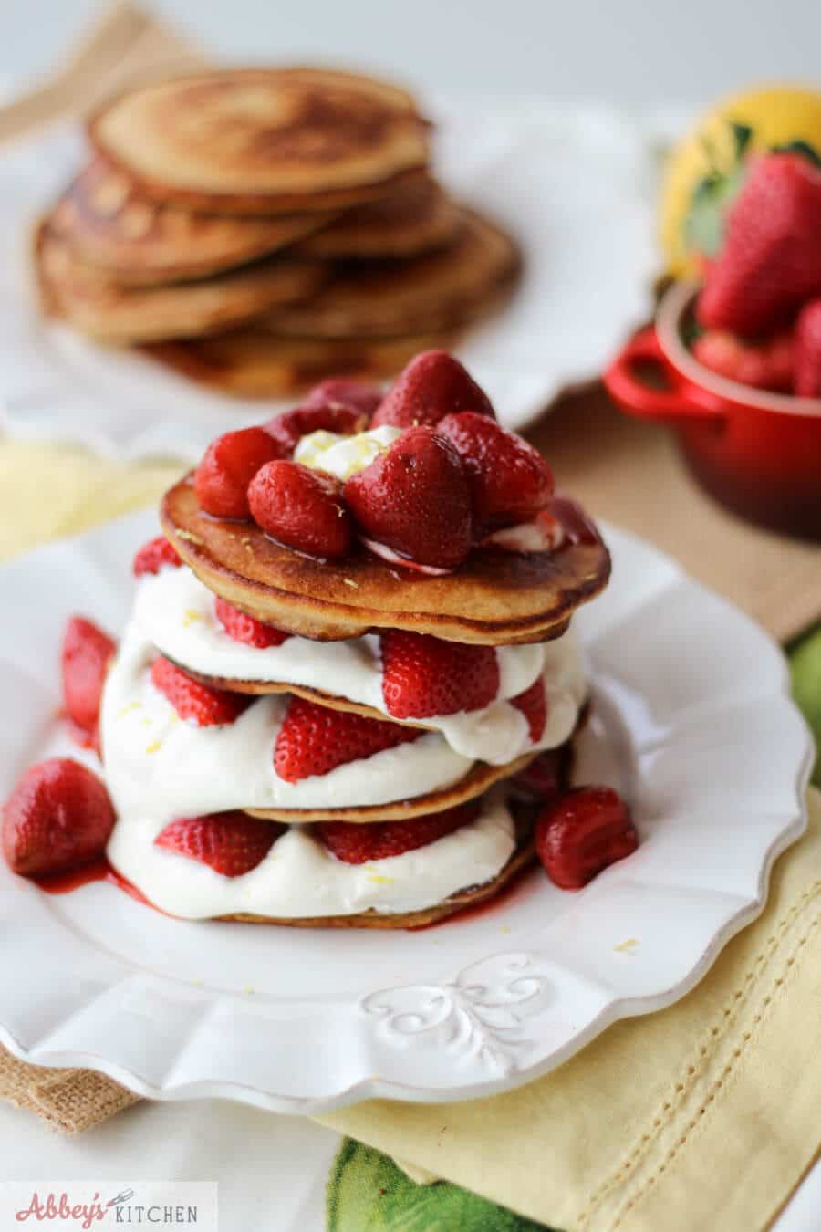 A stack of cheesecake pancakes with strawberries on top on a white plate.