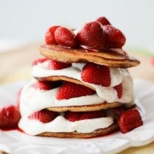 A stack of cheesecake pancakes with strawberries on top on a white plate.