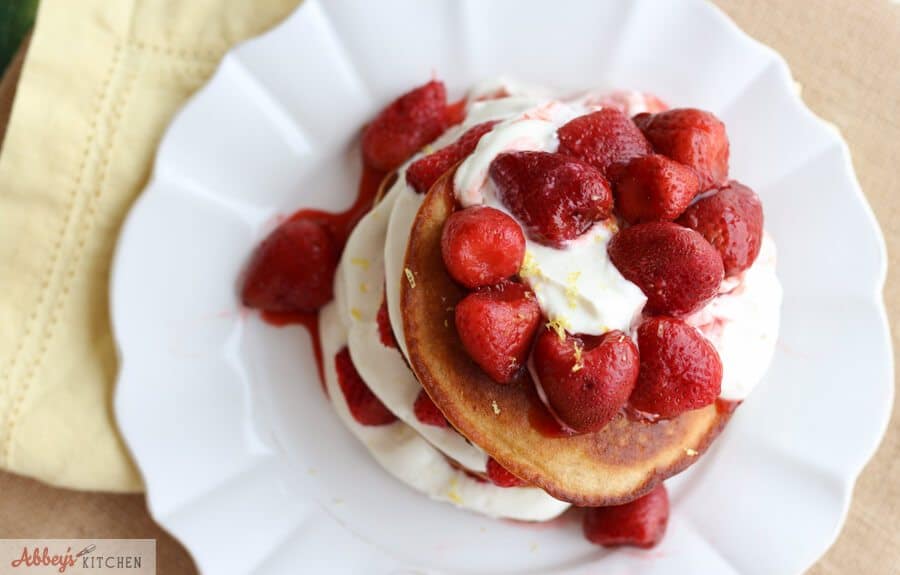 A stack of cheesecake pancakes with strawberries on top on a white plate.