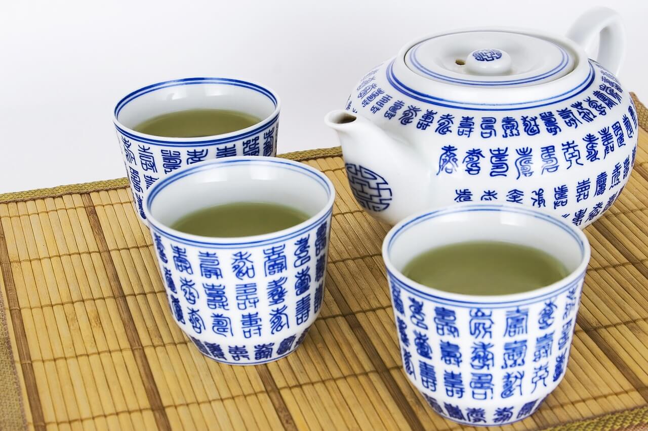 Three cups of green tea beside a teapot.