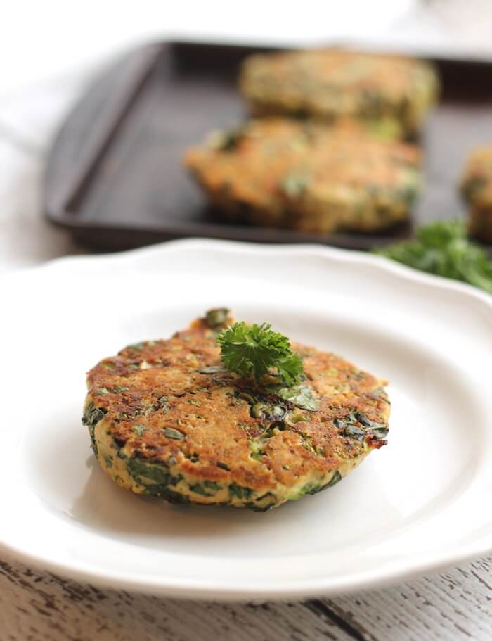 A close up of a kale broccoli salmon burger on a white plate.