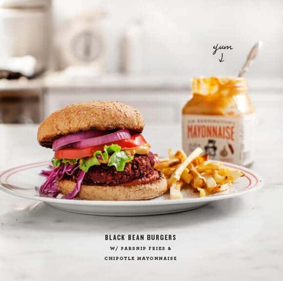 A black bean burger with red onions and tomatoes on a white plate.