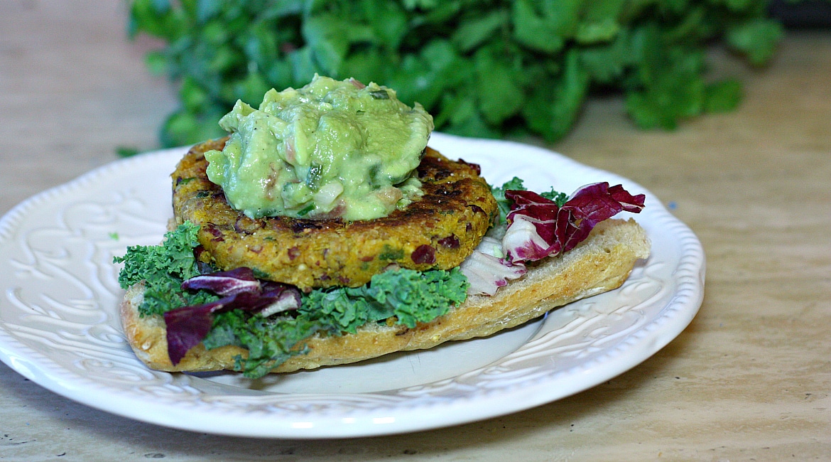 A plate with a pumpkin bean burger with guac on top.