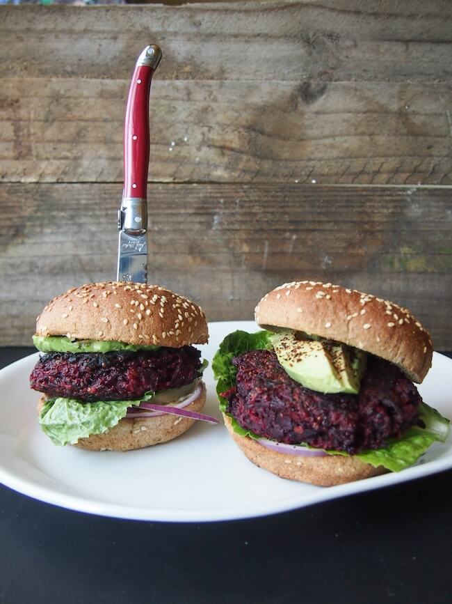 A white plate with two beet burgers, one with a red knife in it.