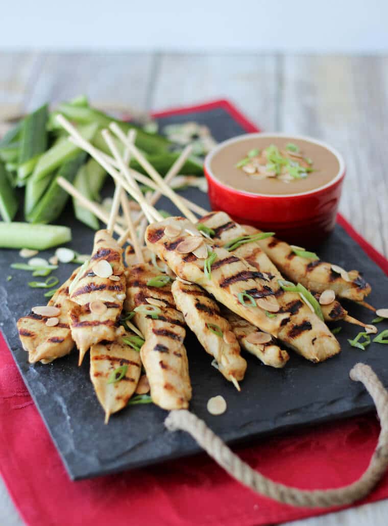 An image of a serving platter of multiple chicken satay with thai almond sauce in the background.