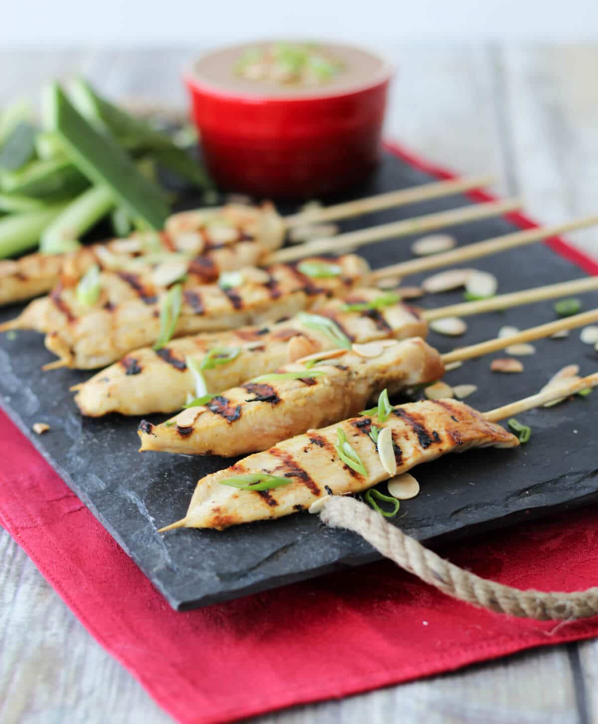 An image of a serving platter of multiple chicken satay with thai almond sauce in the background.