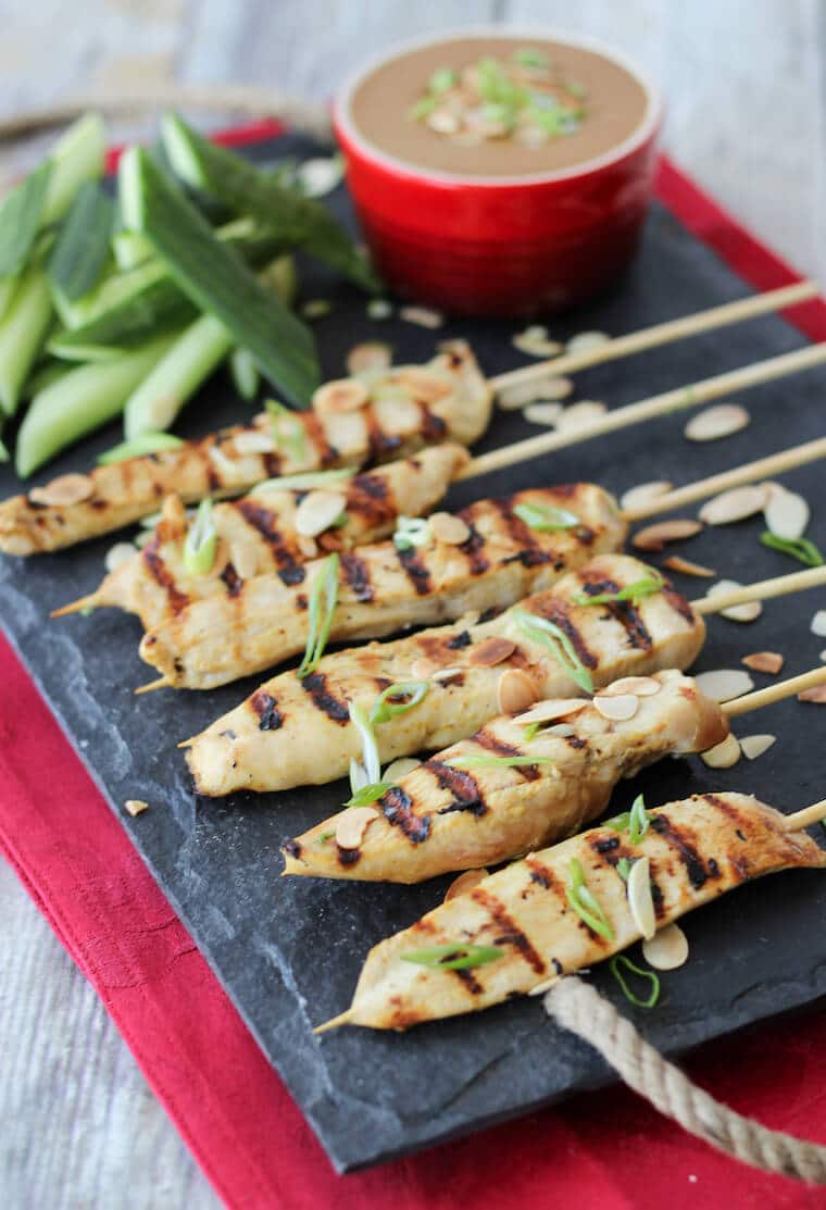 An image of a serving platter of multiple chicken satay with thai almond sauce in the background.