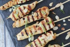 Overhead image of six gluten free chicken satay skewers with green onions on top.