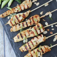 Overhead image of six gluten free chicken satay skewers with green onions on top.