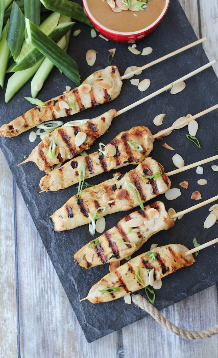 Overhead image of six gluten free satay chicken skewers with green onions on top.