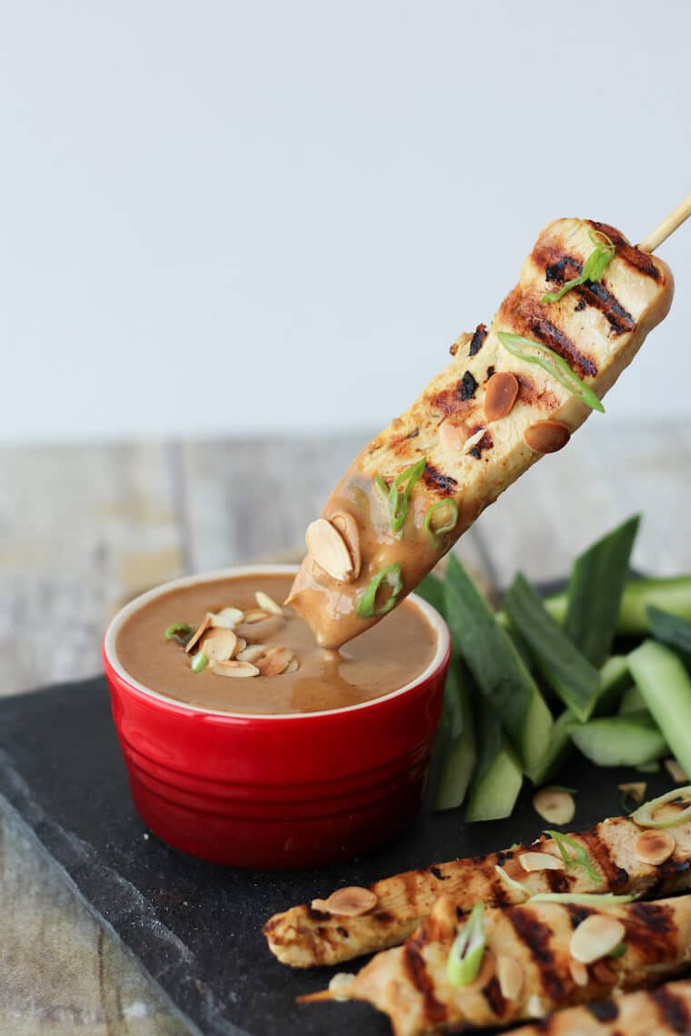 A skewer of chicken satay being dipped in an almond sauce.