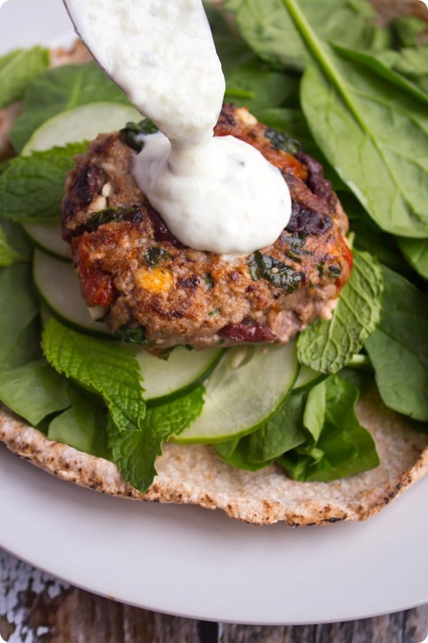 A plate with greek lamb burger with white sauce on top.