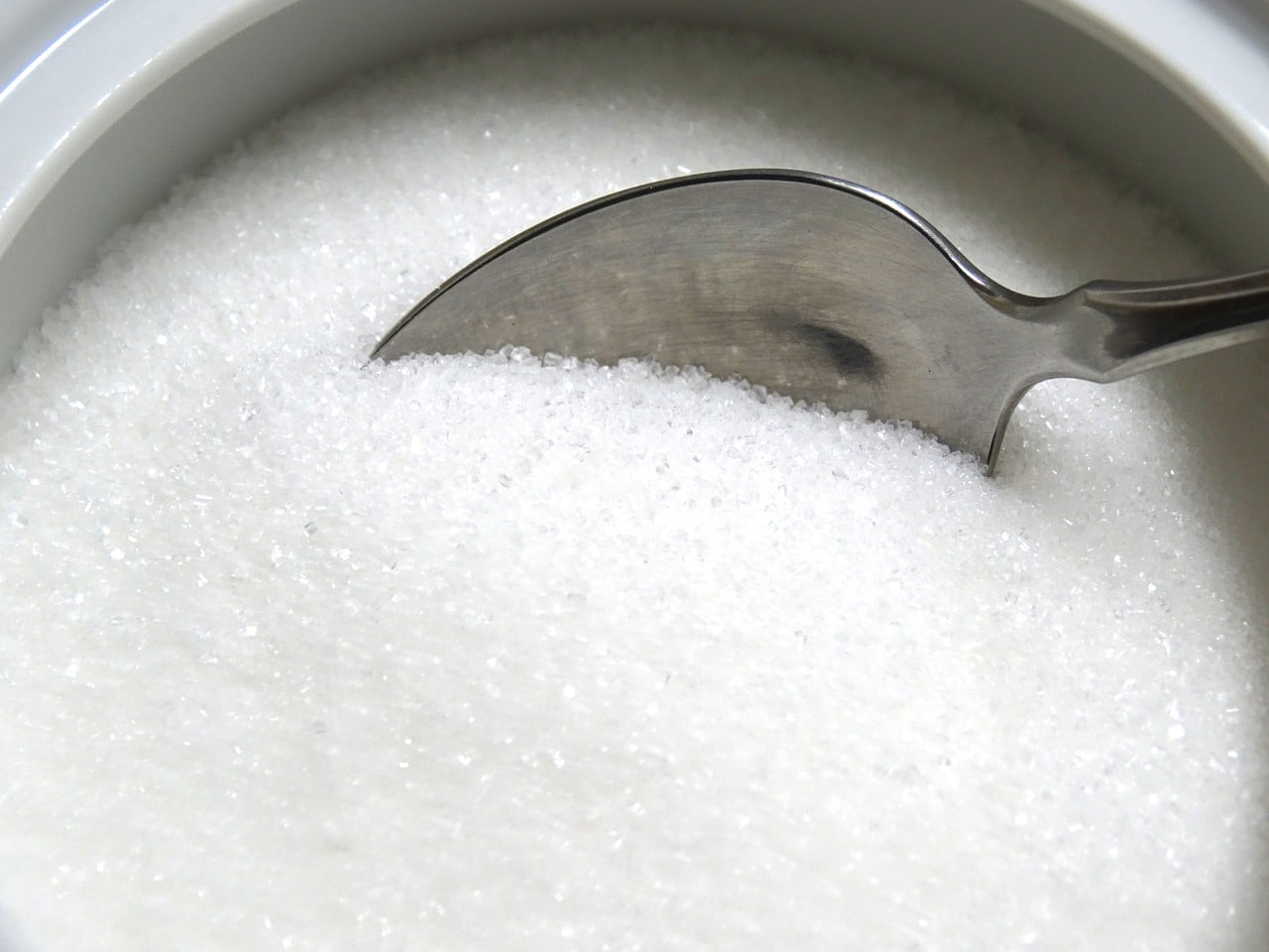 A close up of a bowl of sugar with spoon inside.