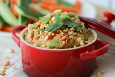 A red bowl of peanut hummus dip with sliced vegetables in the background.