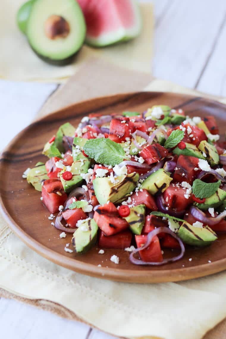 grilled avocado and watermelon salad on a brown plate topped with lime and feta