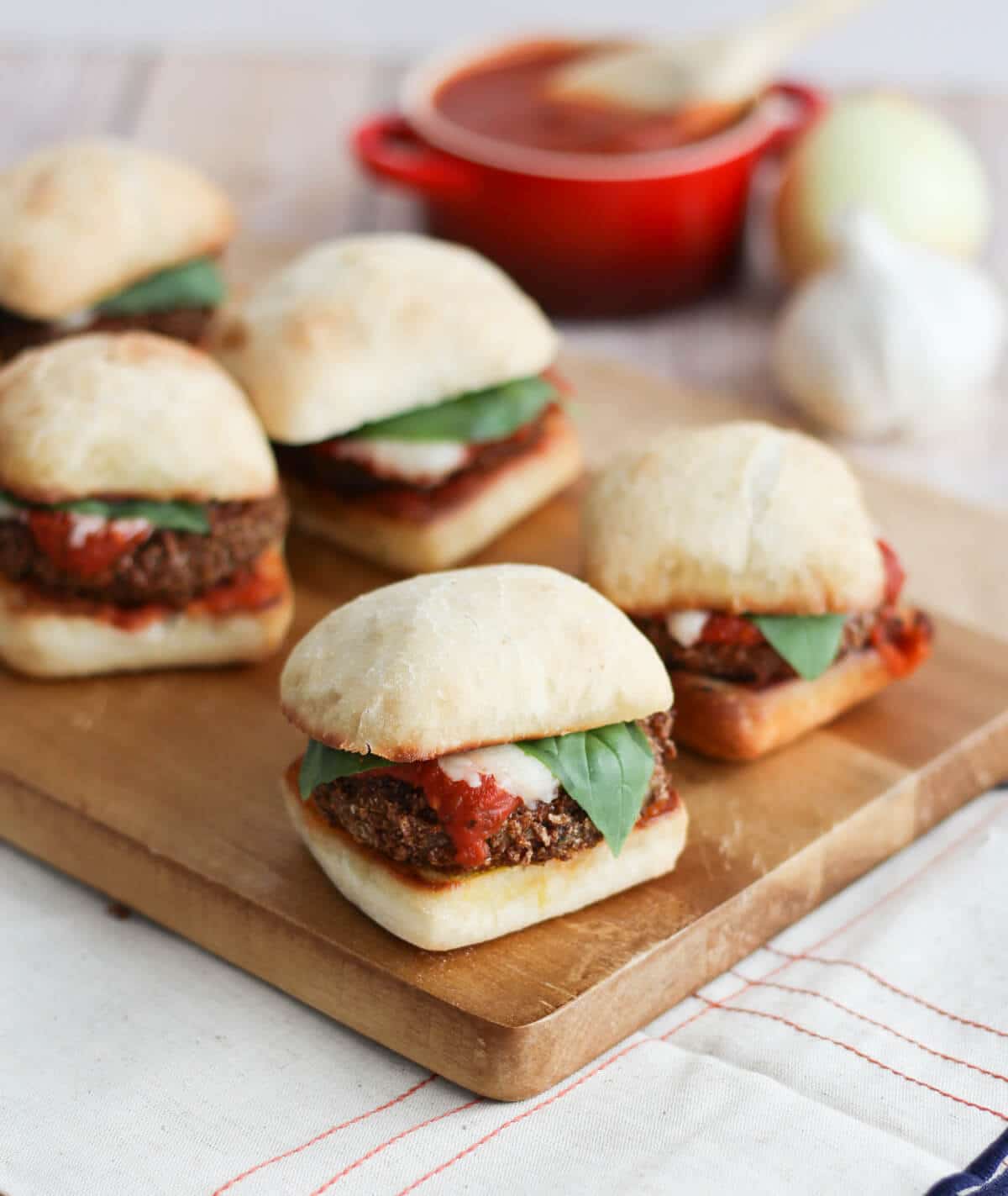 A wooden board with multiple chicken sliders on it.