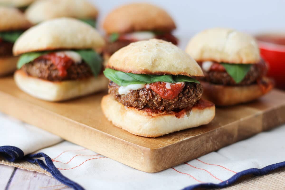 Multiple chicken parmesan sliders on a wooden serving board.