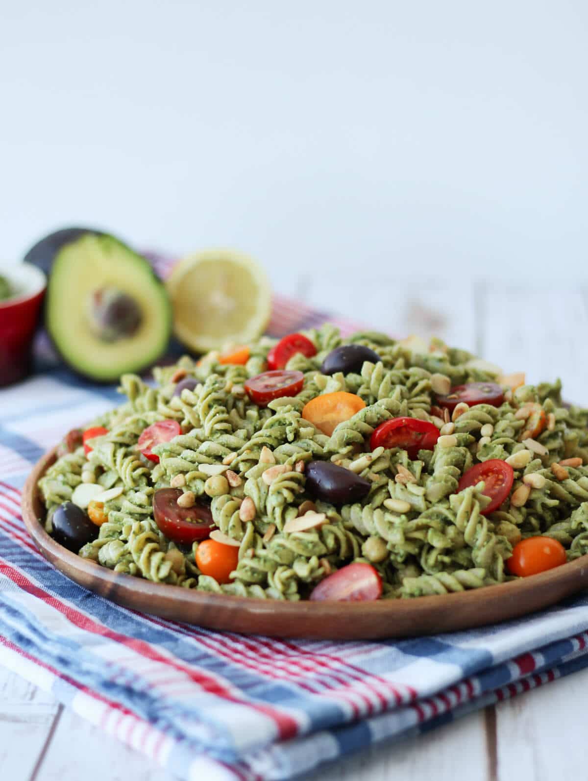 image of green vegan pesto salad with cherry tomatoes on a wooden dish with fresh avocado in the background 