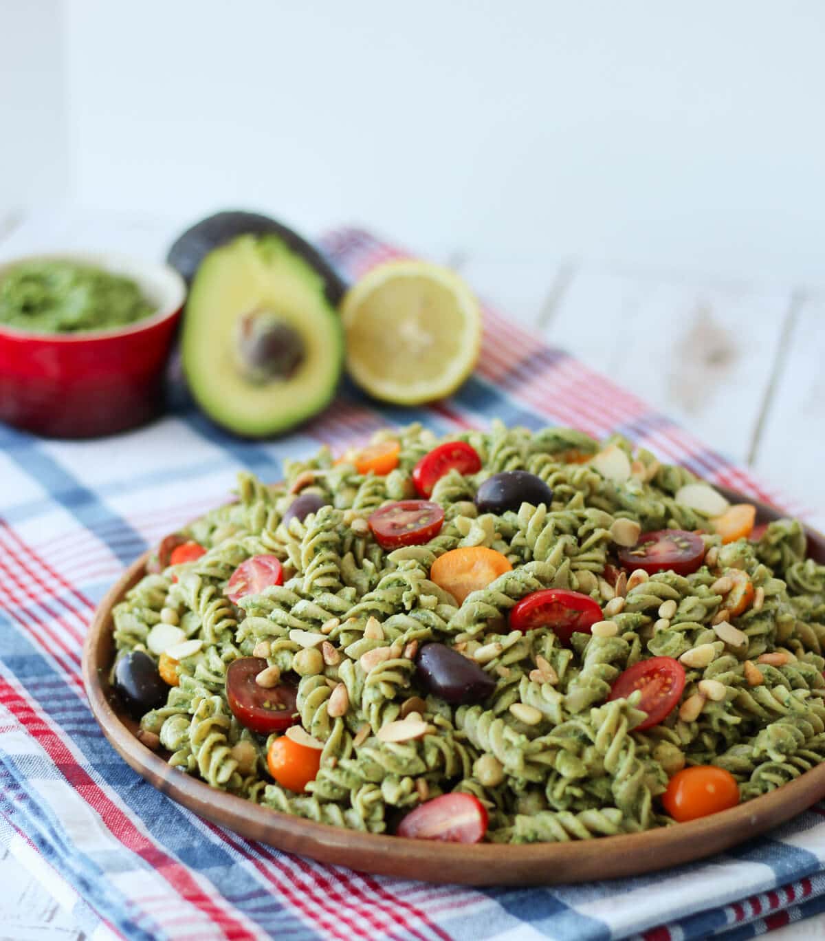 A wooden plate with pesto salad with sliced tomatoes.