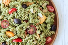 An overhead photo of a vegan pesto pasta salad on a wooden plate.