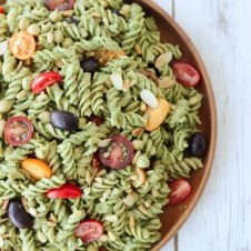 An overhead photo of a vegan pesto pasta salad on a wooden plate.