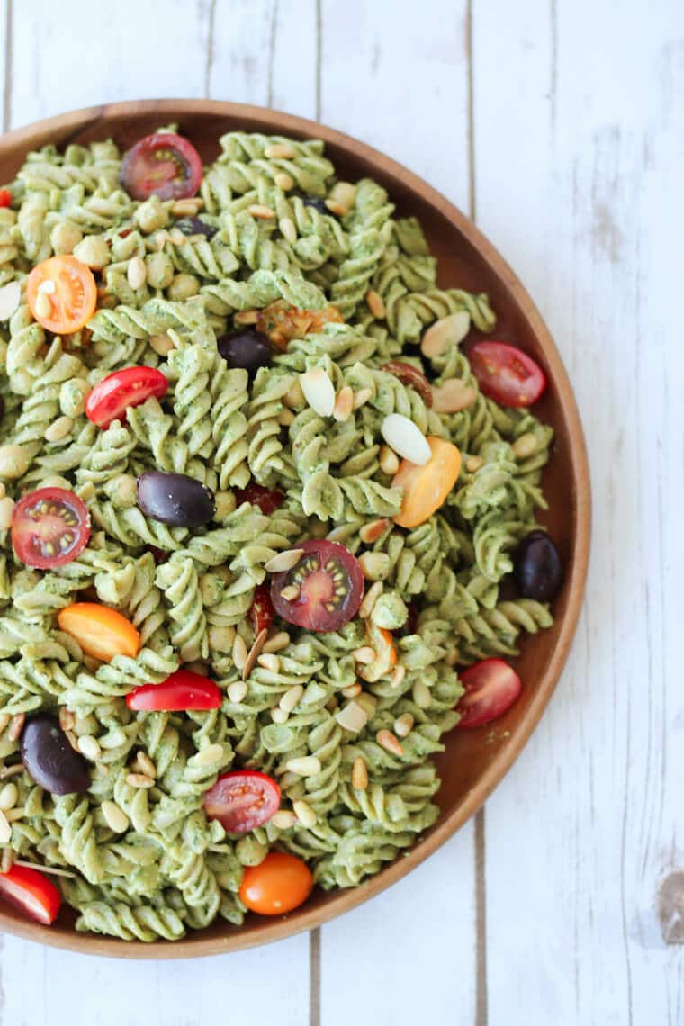 An overhead photo of a vegan pesto pasta salad on a wooden plate.