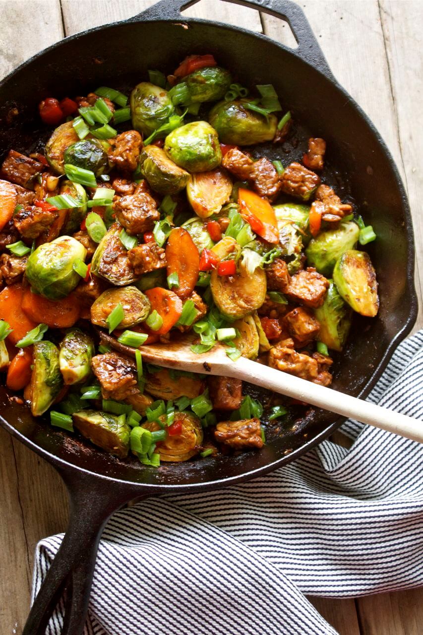 A pan with Brussels sprouts and tempeh stir fry with a spoon inside.