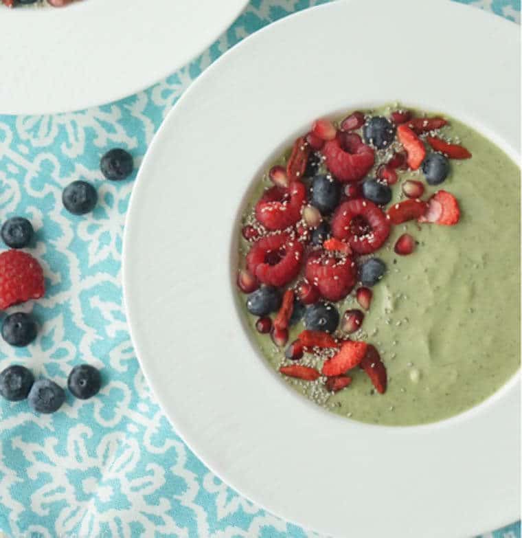 A white bowl containing a green smoothie with fruit on top.