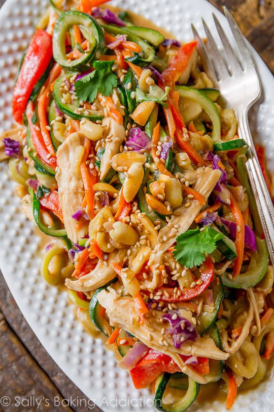 A white plate with peanut chicken zucchini noodles.