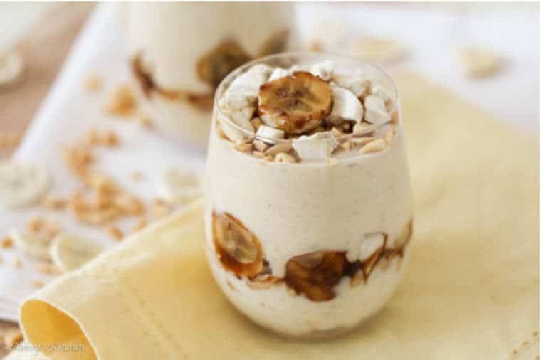 A glass of protein pudding with bananas on top and on the side of the glass.