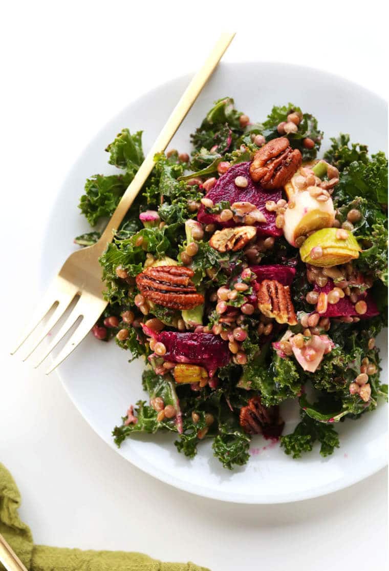 A white plate with salad, pecans, and a fork.