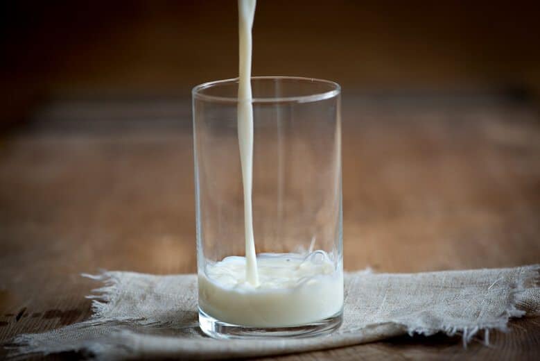 A glass cup with milk being poured in.