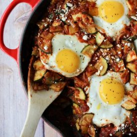 A shakshuka in a skillet with a wooden spoon scooping in.