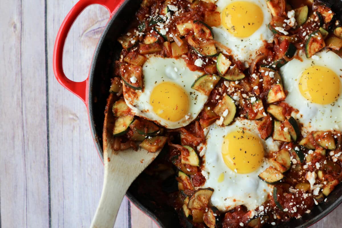 A shakshuka in a skillet with a wooden spoon scooping in.