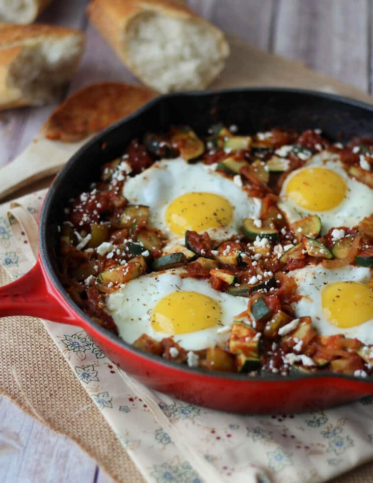 A red skillet containing a gluten free shaksuka with zucchini and feta.