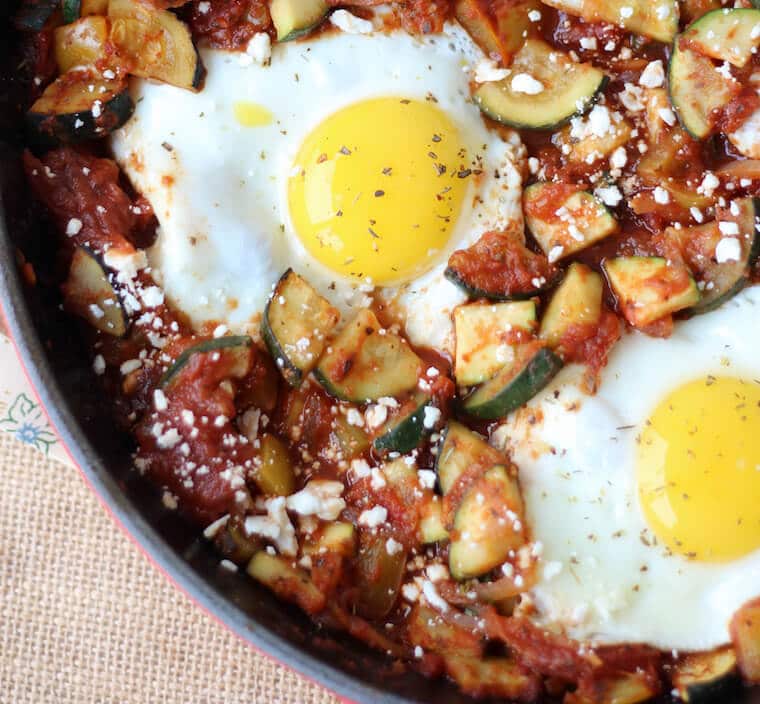 An overhead photo of a skillet containing a gluten free shaksuka with zucchini and feta.