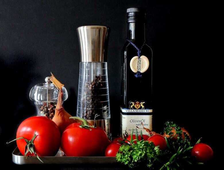 A table with a bottle of olive oil and a black pepper grinder with some fruit in front.