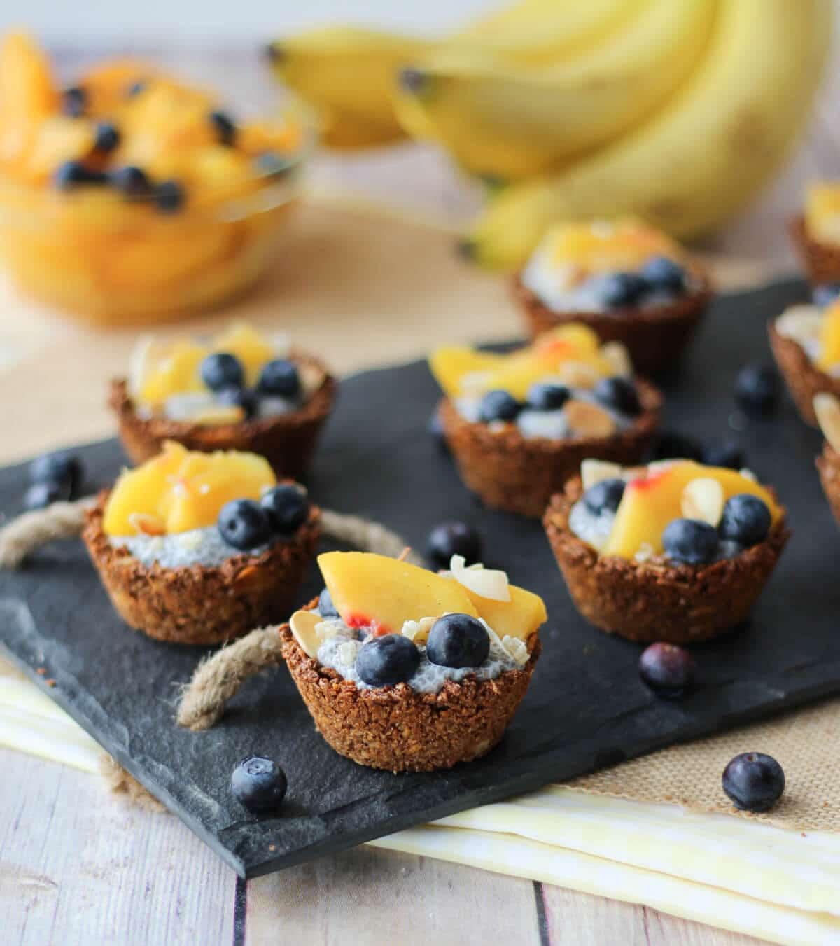 Angled photo of multiple chia pudding granola cups with fresh fruit on top on a black serving platter.
